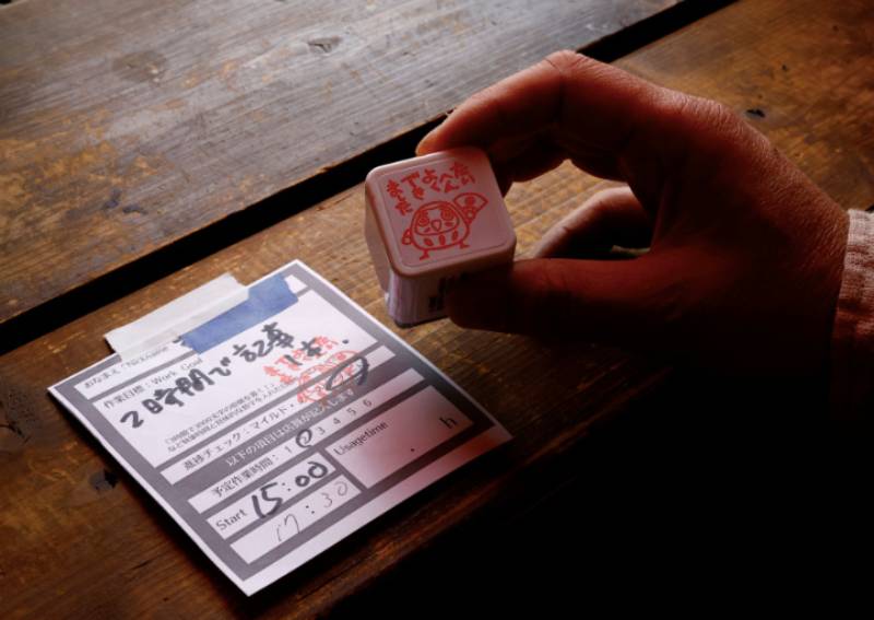 Takuya Kawai, the owner of the Manuscript Writing Cafe which is designed for writers who are working on a deadline, shows a slip of paper on which customers write down goals and the amount of time they plan to finish it in along with a stamp that clears the goal of a customer at the cafe in Tokyo, Japan, April 21, 2022.