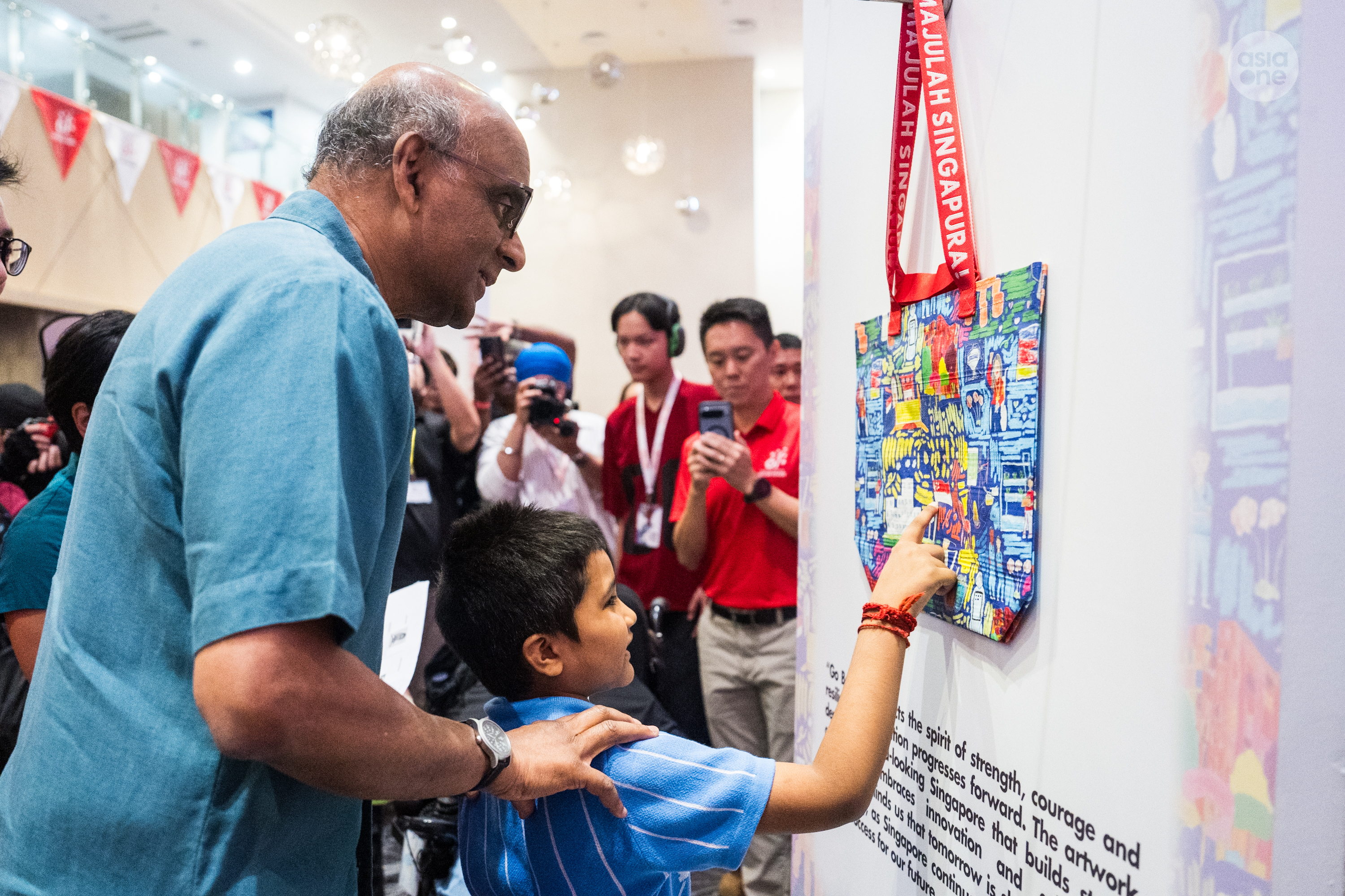 President Tharman Shanmugaratnam listens as one of the artists points out his contribution to the Go Beyond! NDP pack.